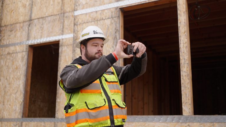 Pacific student Colin Schneider on a construction site, wearing protective gear, takes a photo on his phone.